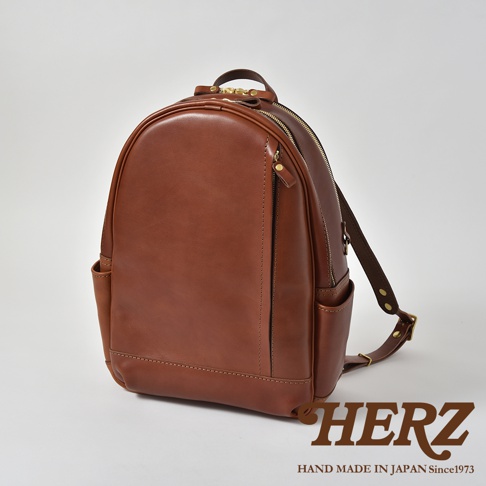 職人手作皮革多功能後背包 R-21，採用光滑棕色皮革製成，設有頂部提把、拉鍊主隔層、前置拉鍊口袋、側邊口袋及可調式肩帶。