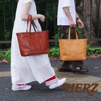 兩款職人手作皮革經典托特包，一款為棕色，一款為卡其色，均為簡約的方型設計，配有雙提把，展現皮革的天然紋理與精緻車縫。