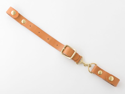 淺棕色皮革製的背包減壓胸前扣帶，配有黃銅色金屬扣環、鉤扣和铆釘。