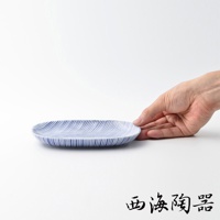 一個藍白條紋的橢圓形陶瓷餐盤，盤面飾有細密的藍色十草紋，由一隻手扶著。
