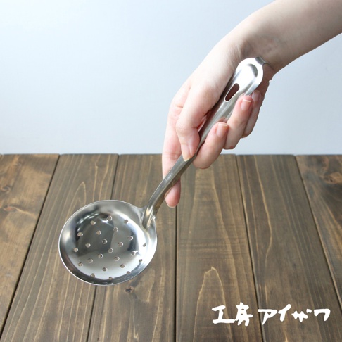一只手持不鏽鋼材質、帶有圓形孔洞的中型撈勺，勺柄上有一個長方形的鏤空設計。