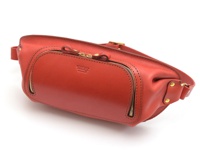 橘紅色皮革製成的職人手作旅行斜背包，設有兩個拉鍊口袋，其中一個較大，並有品牌壓印。包包側邊有鉚釘固定的皮帶連接處，整體呈現圓潤的造型。