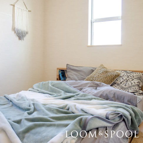 抗菌短絨雙人毯，呈現柔和的淺綠色漸層與白色，材質觸感舒柔。毯子鋪陳在雙人床上，搭配灰色與幾何圖案的枕頭。