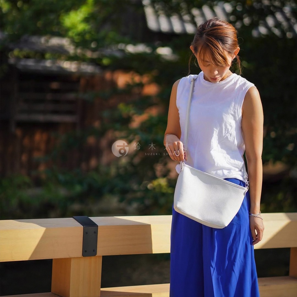 京都職人手作隨身側背包，白色荔枝紋皮革材質，搭配細長同色系的斜背帶，簡約的半月形設計，適合日常攜帶。