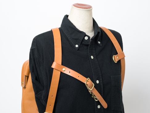 淺棕色皮革製的背包胸前扣帶，寬度約 2.4 公分，附有黃銅扣環、調節扣與 D 型環，展示於黑色襯衫的模特兒身上。