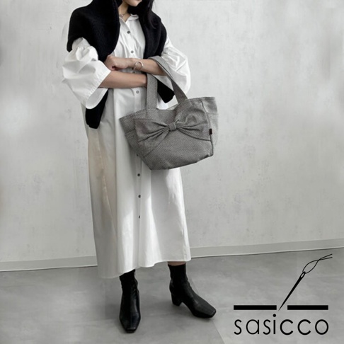 三河木綿刺子織材質的灰色托特包，包身前方有大蝴蝶結裝飾，搭配白色長洋裝與黑色靴子。