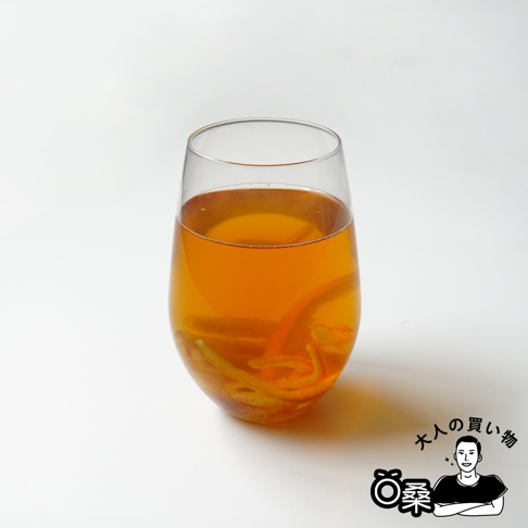 玻璃杯中盛有琥珀色液體，杯內有橙色和黃色的柑橘果皮乾，果皮呈現彎曲的條狀。