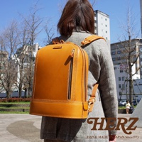 這是一款由 tan 色皮革製成、立體設計的商務後背包。包身線條流暢，配有拉鍊隔層和金屬扣環，展現職人手作質感。