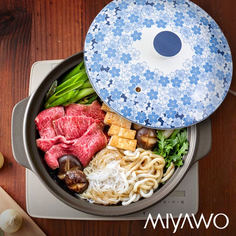 陶土湯鍋內盛有牛肉片、豆腐、香菇、烏龍麵、粉絲和綠葉蔬菜，鍋蓋為白色，印有藍色櫻花圖案，中央有一個藍色圓形把手。