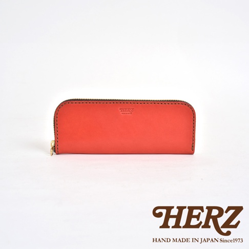 一個亮橘色的皮革筆袋，拉鍊開合，上面壓印有HERZ字樣及Made in Japan字樣，下方另有HERZ品牌標誌與Hand Made in Japan Since 1973字樣。