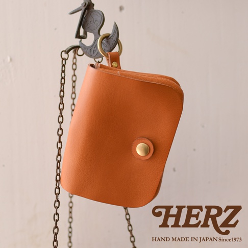 職人手作皮革旅行用雙層錢包，呈現天然皮革的棕褐色，配有金色按扣，透過金屬鏈條懸掛。