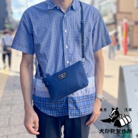 深藍色刺子織隨身斜背包，斜挎於身穿藍色格紋襯衫的男子身上，包包上有品牌標籤。