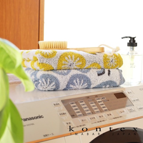 在洗衣機上方堆疊的兩條毛巾，一條為黃色花朵圖案，另一條為藍色花朵圖案，旁邊有洗碗精瓶和木質毛巾架。