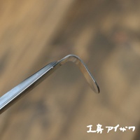 不鏽鋼中型撈勺的彎曲勺頭特寫，呈現金屬光澤，背景為模糊的木紋。