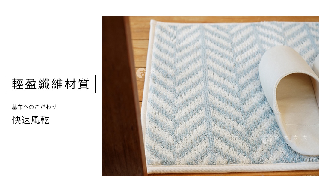 淺藍與白色相間的chevron圖案地墊，材質為柔軟的織品，邊緣有白色包邊。一隻淺米色的拖鞋放在地墊的一角。