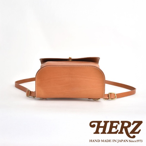 職人手作皮革翻蓋迷你後背包，採用天然皮革材質，呈現溫潤的淺棕色調。包身線條圓潤，搭配簡約的翻蓋設計與金屬扣環，展現經典質感。