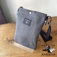 灰色帆布平板收納側背包，包身帶有品牌標籤，下方另有品牌標誌與文字。