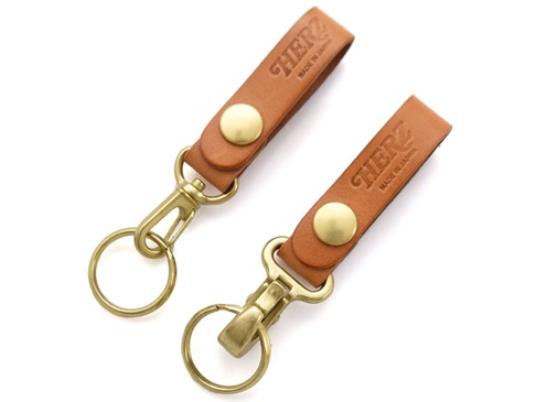 兩個棕色皮革製的鉤扣鑰匙圈，帶有金色金屬鉤扣和鑰匙環，皮革上壓印有「HERZ」和「MADE IN JAPAN」字樣。