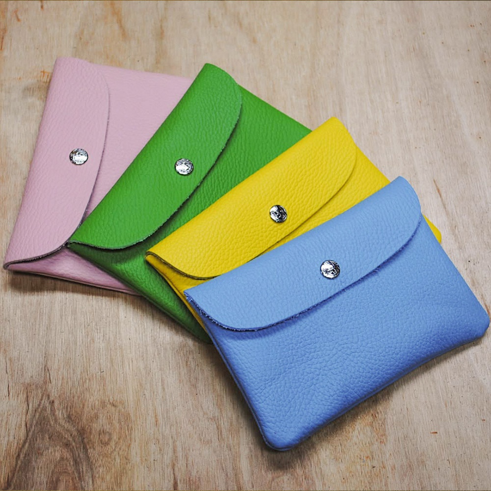 四個顏色各異的皮革小收納包，分別為粉紅色、綠色、黃色和藍色，皆配有銀色按扣。