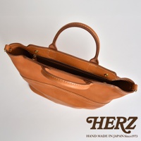 棕色皮革兩用托特包，設有提把和拉鍊開合，包身以白色縫線裝飾，整體呈現簡約風格。