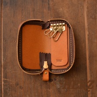 一個棕色皮革製成的鑰匙包，打開狀態，露出內部四個金屬掛鉤和皮革拉鍊。