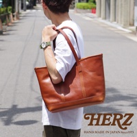 職人手作皮革經典托特包，採用光滑棕色皮革製作，配有兩條皮革提把，包身縫線明顯，質感樸實，展現經典設計。