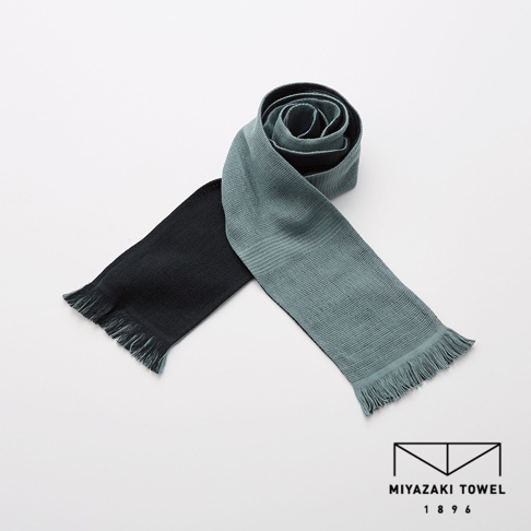 今治匹馬棉雙色圍巾，一端為黑色，另一端為淺藍綠色，兩端皆有流蘇，材質觸感柔軟。