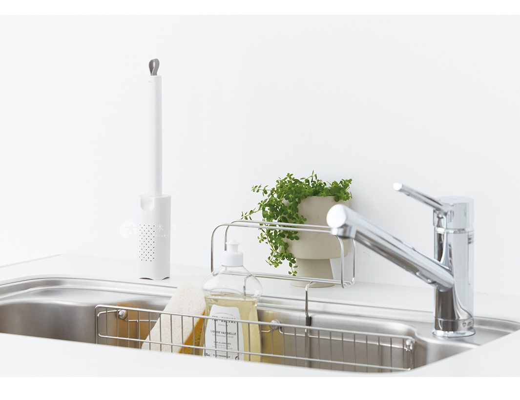 一個白色推拉式海綿刷，置於水槽旁，旁邊有洗潔精瓶、海綿和一盆小型綠植。