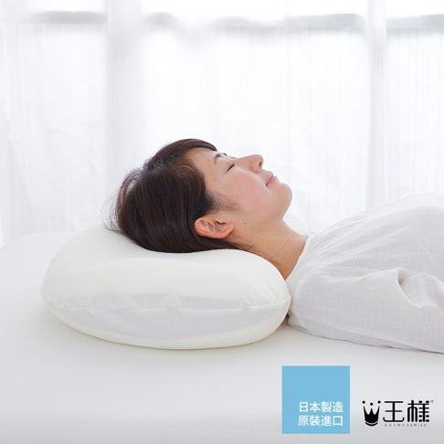 一名女性仰躺在白色床鋪上，頭部枕在一個白色的、具有弧度的「王樣の雲上枕」上。枕頭材質看起來柔軟，輪廓清晰。