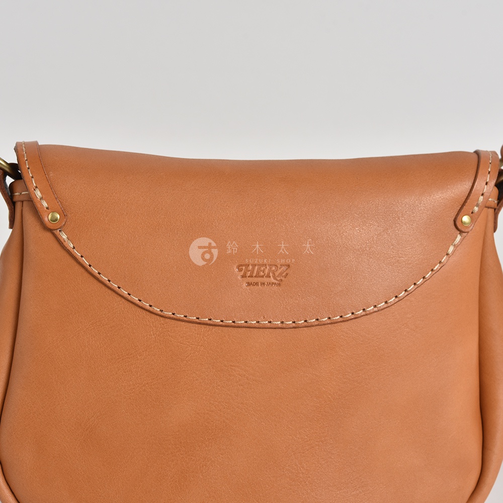 駝色皮革休閒旅行馬鞍包，正面壓印有HERZ品牌標誌，標示made in JAPAN。