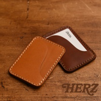 兩個皮革名片夾，一個為淺棕色，一個為深棕色，以斜視角呈現於木質背景上。