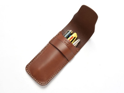 棕色皮革製成的鋼筆收納套，內含三支筆，其中一支為銀色，一支為黃色，一支為綠色。收納套有縫線細節，並有一個皮革袢帶固定。