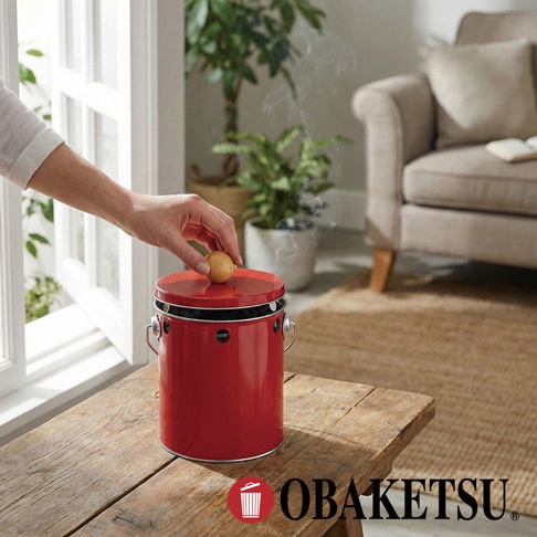 OBAKETSU 紅色手工製蚊香桶，頂部有一個圓形木蓋，有煙從桶中冒出，放在木桌上。