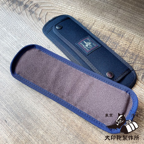 深藍色純棉帆布製成的肩墊，內部襯有紫色絨布，配有金屬按扣，外側印有品牌標誌。