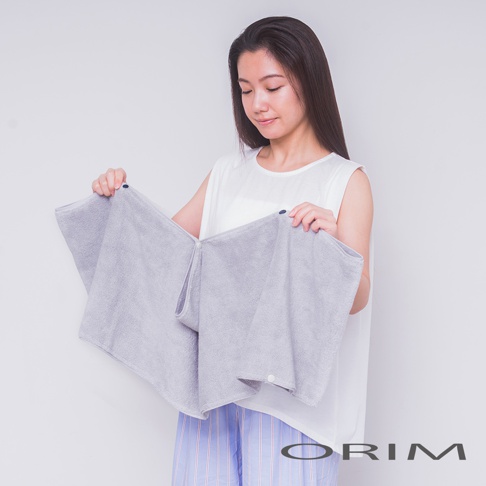 一位女性手持淺灰色、柔軟材質的吸水頭巾，頭巾展開呈現扇形，中央有按扣設計，可見其吸濕速乾的特性。