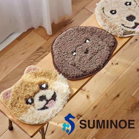 三款造型可愛的 SUMINOE 狗狗造型椅墊並排放置在木質長凳上，從左至右分別為具有立體毛絨質感、露出粉色舌頭的棕色狗狗造型椅墊，中間為深棕色圓形捲毛椅墊，右側則為另一款淺色系狗狗頭部造型椅墊，整體畫面充滿溫馨居家風格。