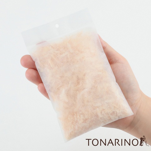 一隻手拿著一個半透明的白色防潮消臭檜木除濕包，包內裝滿了淺棕色的檜木碎屑。