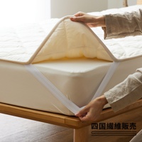 雙人加大床墊，奶油色，表面有菱格紋縫線，邊緣為米色滾邊。床墊有四個鬆緊帶固定在床墊上。