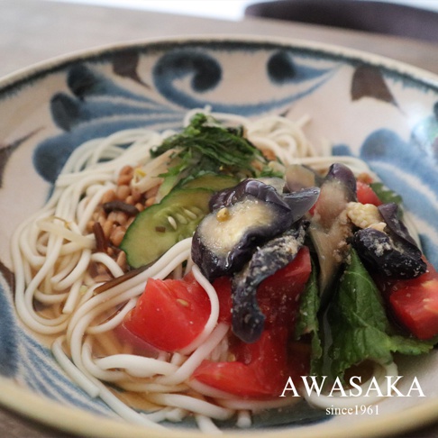 青釉繪寬口丼碗盛裝著白麵，碗內有茄子、番茄、小黃瓜、豆芽菜及綠色蔬菜，碗緣繪有藍色植物紋飾。