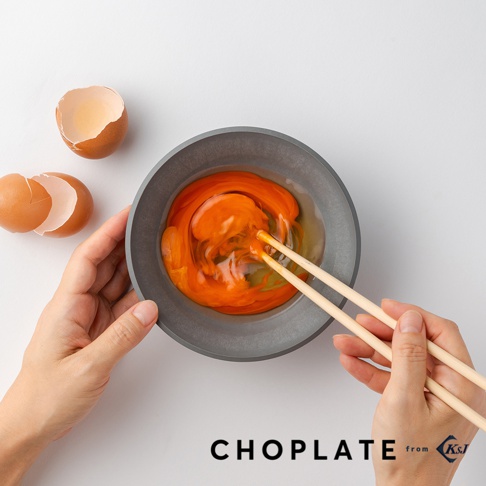 灰色CHOPLATE沙拉碗內裝有攪拌中的蛋黃，碗旁有兩半雞蛋殼。一雙淺木色筷子正攪拌碗內的蛋黃。