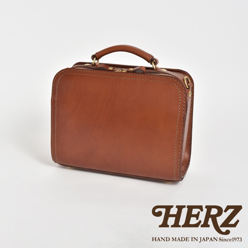 棕色皮革製成的方形單肩包，配有頂部提把、拉鍊開合和縫線細節。