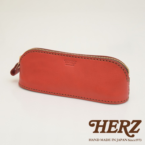 職人手作皮革三角弧形收納筆袋，橘紅色皮革，金色拉鍊，手工縫線，品牌標誌壓印。