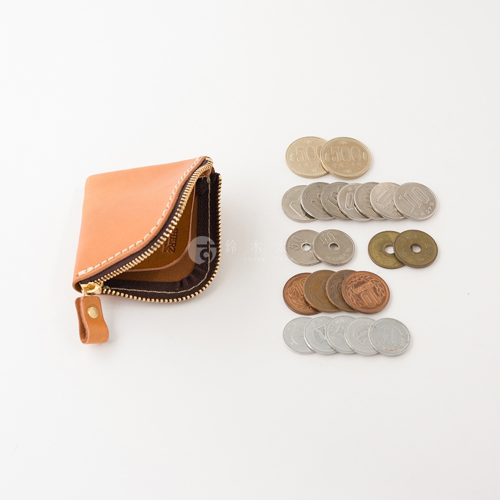 一個淺棕色的日本HERZ職人手作皮革零錢包，造型精巧簡約，拉鍊開口處呈現敞開狀，旁邊整齊排列著多枚不同面額的日本硬幣，整體以高雅的手工質感呈現，背景為純白。