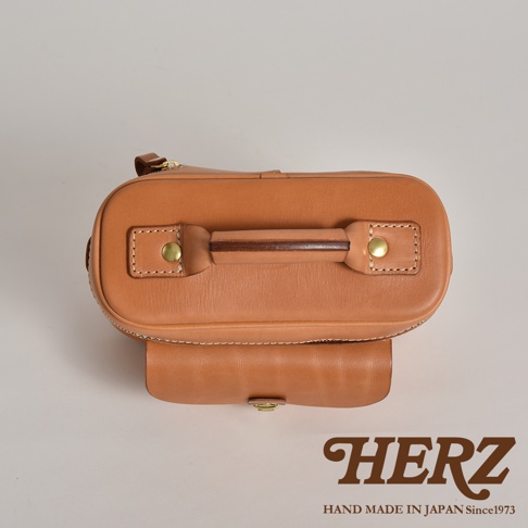 職人手作皮革軟皮相機包 N-6，呈現溫潤的淺棕色調。包體由光滑的皮革製成，頂部設有堅固的提把，並以銅扣固定。包身側面有拉鍊設計，正面有一個帶有金屬釦的翻蓋口袋。