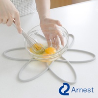 灰色矽膠鍋具防刮保護墊，呈花朵狀，上面放著一個裝有雞蛋的玻璃碗，有人正在用打蛋器攪拌。