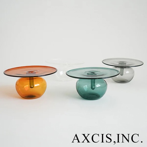 AXCIS, INC. 的 Lua 線香玻璃花器，以橙色、藍綠色和煙灰色呈現，簡約的設計帶有圓潤的底座和扁平的托盤。