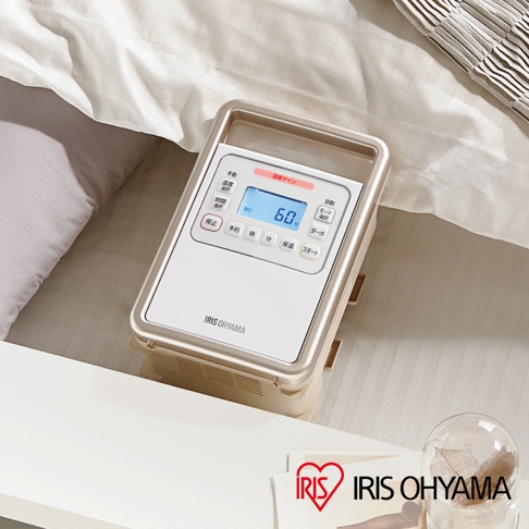 白色與金色邊框的IRIS OHYAMA強力被褥乾燥機，面板上有日文顯示與數字「60」，裝置放置於床鋪旁。