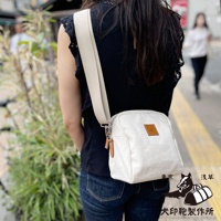 一位女士身穿黑色上衣和牛仔褲，側背一個白色石洗帆布散步包，包包上有一個皮革標籤，旁有東京淺草犬印製作所的圖案。