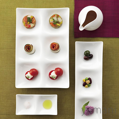 白色陶瓷三格小菜盤，其中一格盛有兩顆番茄起司，另兩格各有一捲蔬菜，最上方兩格各有一份色彩豐富的凍狀小點。旁邊另有兩格小盤，一格盛有鹽粒，一格盛有橄欖油。右側有一長條三格盤，盛有橄欖、豆子混合物及紫色花椰菜。