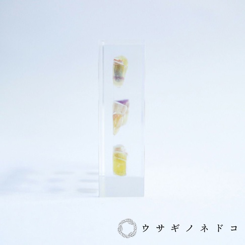 透明壓克力塊中垂直排列著三塊帶有黃色、紫色和粉色色塊的螢石切片標本。